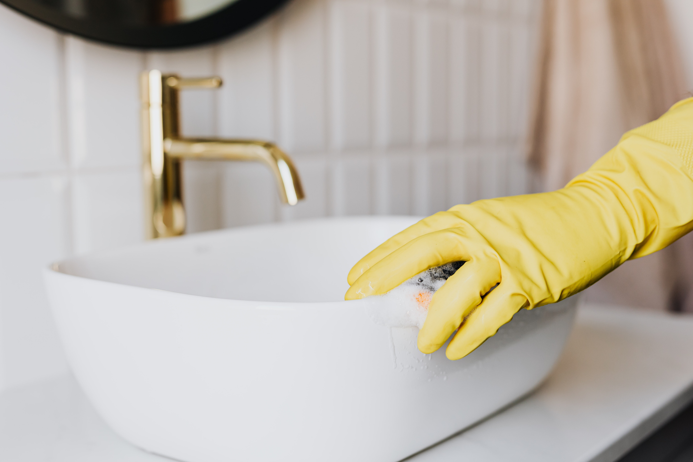 Person in glove cleaning bathroom sink